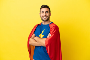 Young handsome caucasian man isolated on yellow background in superhero costume with arms crossed