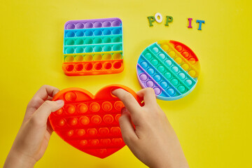 Kid hands playing with colorful pop It fidget toy. Colorful antistress sensory toy fidget push pop it.