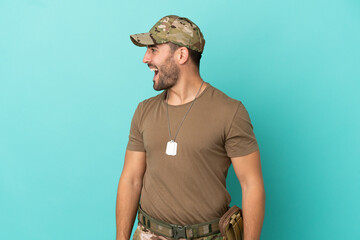 Military with dog tag over isolated on blue background laughing in lateral position