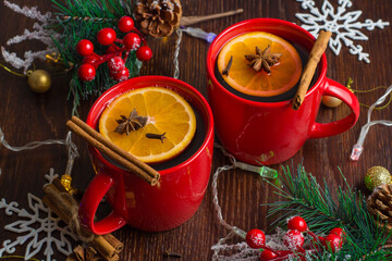 Aromatic, hot and delicious mulled wine with orange, cinnamon, star anise and cloves in red cups with Christmas decor. Feeling of celebration and warmth in the house