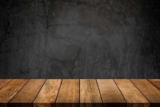 Wooden table top with dark concrete polished wall blurred background. Copy space for your display or montage product design.