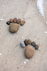 The stones are arranged in the form of feet on sandy beach.