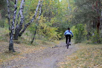 Fototapeta premium The girl rides a mountain bike along a trail in the forest. Outdoor training and sports. Active and healthy lifestyle.