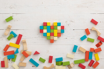 Top view of colorful wooden toy blocks on white wooden table background. The cubes are assembled in the shape of a heart. Natural materials. Healthy childhood. Learning and education concept.