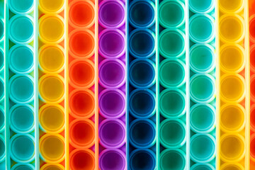 Bright rainbow toy antistress for children and adults on a colorful background. Flexible sensory antistress toy - popit.
