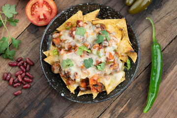 A plate of delicious corn chips nachos in cheddar cheese with beans, tomato, green chili, black...