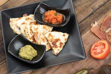 A toasted tortilla with chicken, peppers, red onion and mozzarella served with a guacamole dip and sour cream isolated on wooden table