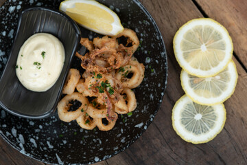 A plate of crunchy deep fried squid rings, calamari with  smoky red bell pepper, almond, cherry vinegar, tomato and cayenne served with tartar sauce dip on the side isolated on wooden table