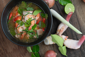 Traditional spicy prawn soup with galangal, lemongrass, kaffir lime leaf and straw mushrooms isolated on the wooden table