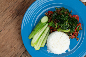 Rice with stir-fried minced pork and basil with cucumber isolated on wooden rustic table