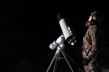 A man stands next to a telescope against a dark background.