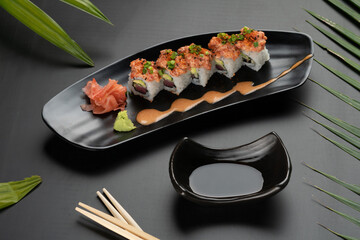 Sushi Roll - Maki Sushi made of tuna, avocado, mayonnaise and ebiko sushi isolated on black table with tropical leaves