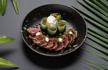 Seared tuna sesame and fresh spring rolls with ginger sesame soy sauce isolated on black table with tropical leaves