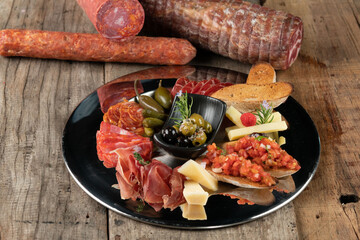 An assortment of cold appetizers served on a black plate isolated on rustic wooden table