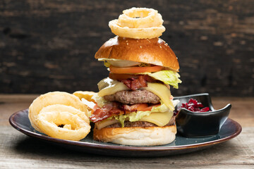 Big burger with beef, bacon, tomato, cheese, lettuce and onion served with french fries, onion rings and beetroot salad on the side isolated on rustic wooden table