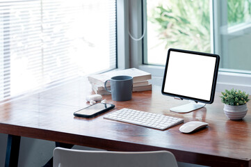 Mockup blank screen tablet on stand with keyboard and gadget on wooden table in modern office room.
