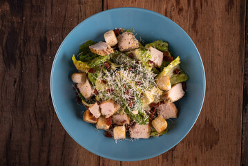 Top view of chicken Cesar salad with croutons and grated cheese isolated on wooden rustic table