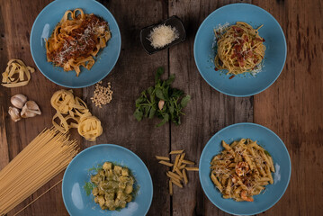 Top view variety of homemade prepared pasta isolated on wooden table. Penne aglio e olio prawn, spaghetti carbonara, fettuccini Bolognese and gnocchi pesto