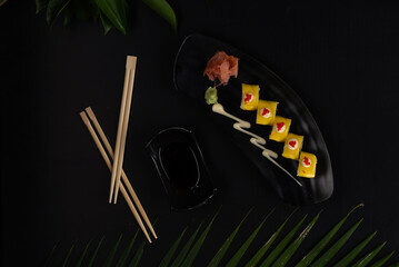 Top view of deep-fried soft-shell crab, cucumber, mango, mayonnaise and tobiko isolated on black table with tropical leaves
