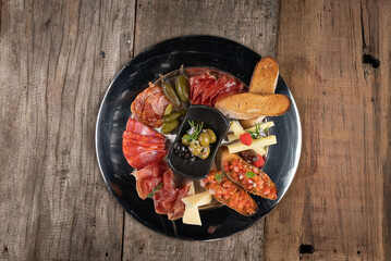 Top view of an assortment of cold appetizers served on a black plate isolated on rustic wooden table