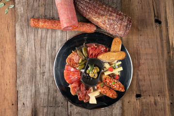 Top view of an assortment of cold appetizers served on a black plate isolated on rustic wooden table