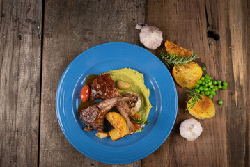 Top view of two grilled lamb chops and potatoes served on pea puree with a mint sauce isolated on rustic wooden table