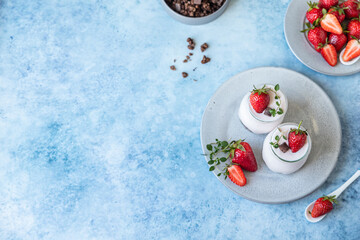 Fototapeta na wymiar Two jars with yoghurt, chocolate granola and fresh strawberries on ceramic plate, blue concrete background. 
