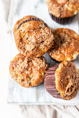 Tasty breakfast muffins with oat crumbs topping on white cutting board, light concrete background. 
