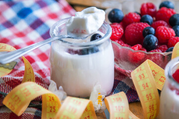yogurt with raspberries and blueberries on wooden background with measuring tape, diet and food concept