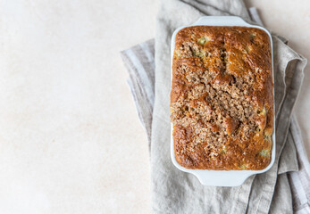 White ceramic baking dish with healthy vegan crumble cake, light concrete background. Healthy dessert. Top view. Copy space.