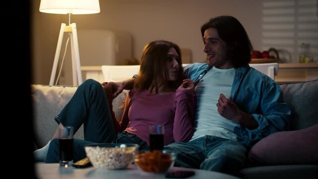 Cozy evening at home. Young happy man and woman sitting on sofa, joking and laughing, enjoying time together