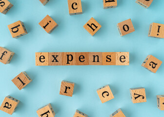 Expense word on wooden block. Flat lay view on blue background.