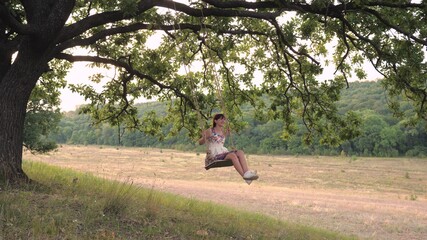 An adult girl swinging on a swing tied to a tree in nature, rolling soaring in the air in the wind and laughing, the concept of a happy life
