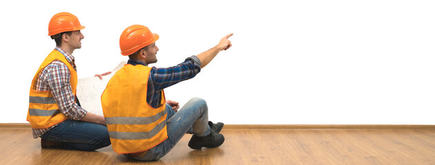 The two builders with a paper sit on the floor on the white wall background