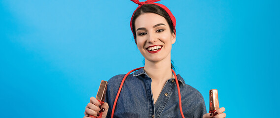 The happy woman holding jumper cables on the blue background