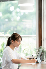 Portrait of young beautiful asian woman using computer for her online leraning while staying at home.