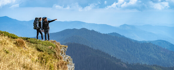 The man and a woman gesturing on the cliff with a beautiful view - obrazy, fototapety, plakaty