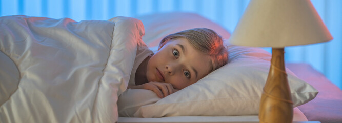 The frightened girl lay on the bed. Evening night time
