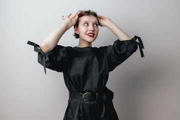 A fashionable beautiful girl in a black dress, adjusts her sunglasses. white background