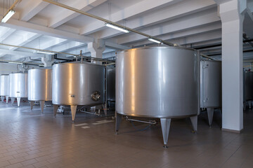 Fototapeta na wymiar Stainless steel barrels and tanks and other containers for liquids in the food industry. Industrial production of alcoholic or soft drinks.