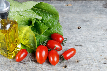 古い木のテーブルを背景に置かれたミニトマトとオリーブオイルとロメインレタス