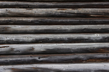 The wall of an old wooden house made of darkened weathered logs. Traditional Russian log hut.