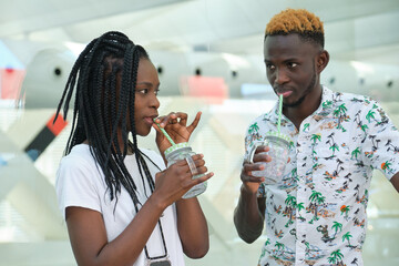 Stylish african couple drinking refreshing drinks at street. Summertime concept.