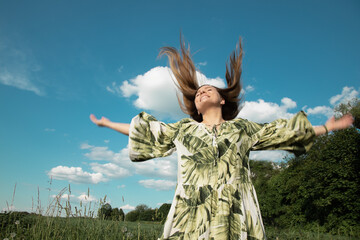 young woman in a dress in green field with outstretched hands toblue sky and sun, flying hair....