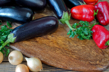 Whole raw eggplant, onions, red bell pepper and parsley on wooden cutting board.