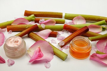 Body care cosmetics based on rhubarb and rose. Rhubarb stalks and rose petals lie on the table.