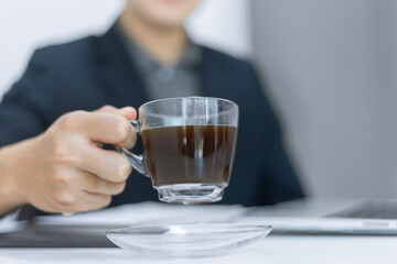 Business partners concept a young male entrepreneur holding a cup of black coffee sitting with a laptop while attending in a monthly meeting