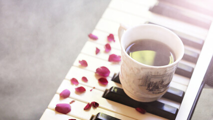 A cup of coffee on the piano and pink rose petals