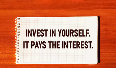 the text INVEST IN YOURSELF, IT PAYS THE INTEREST is written on a notebook and a wooden table. Invest in yourself, motivation to take action.