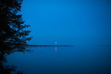 Rise of a bloody, red, moon, full moon, over a large river at night
